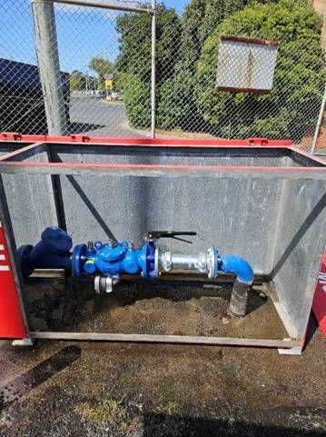 A blue pipe is sitting inside of a metal box next to a chain link fence.
