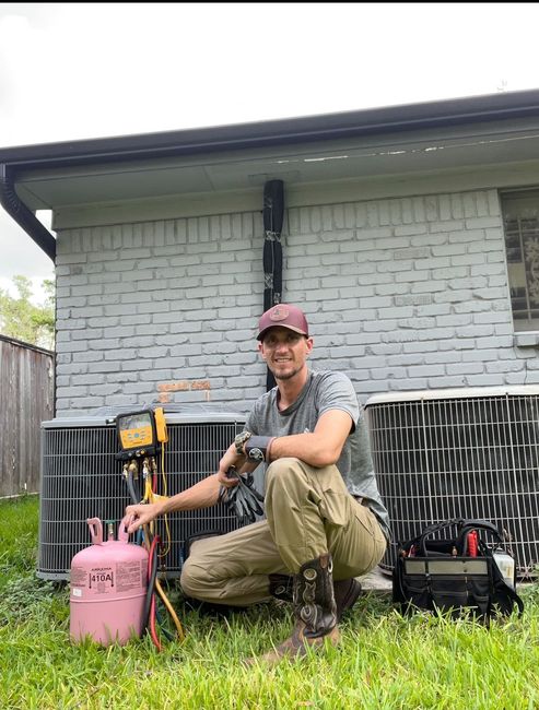 An HVAC technician is kneeling down in front of an air conditioner working on Condenser unit