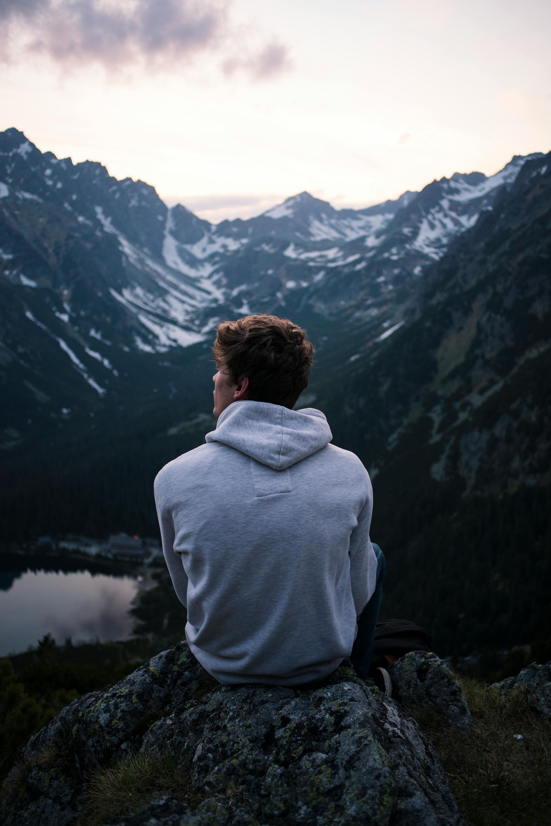 A man is sitting on top of a mountain looking at the mountains.