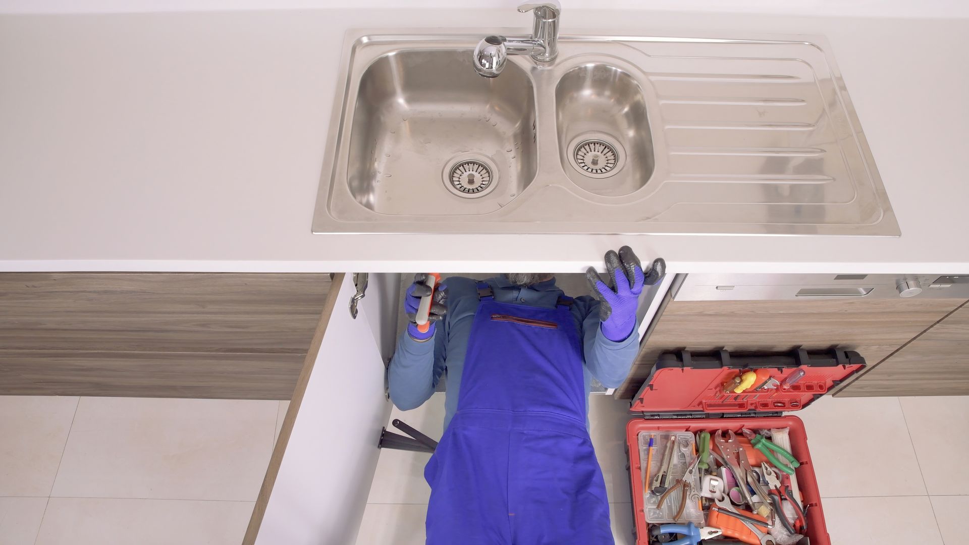 A plumber is working under a kitchen sink.