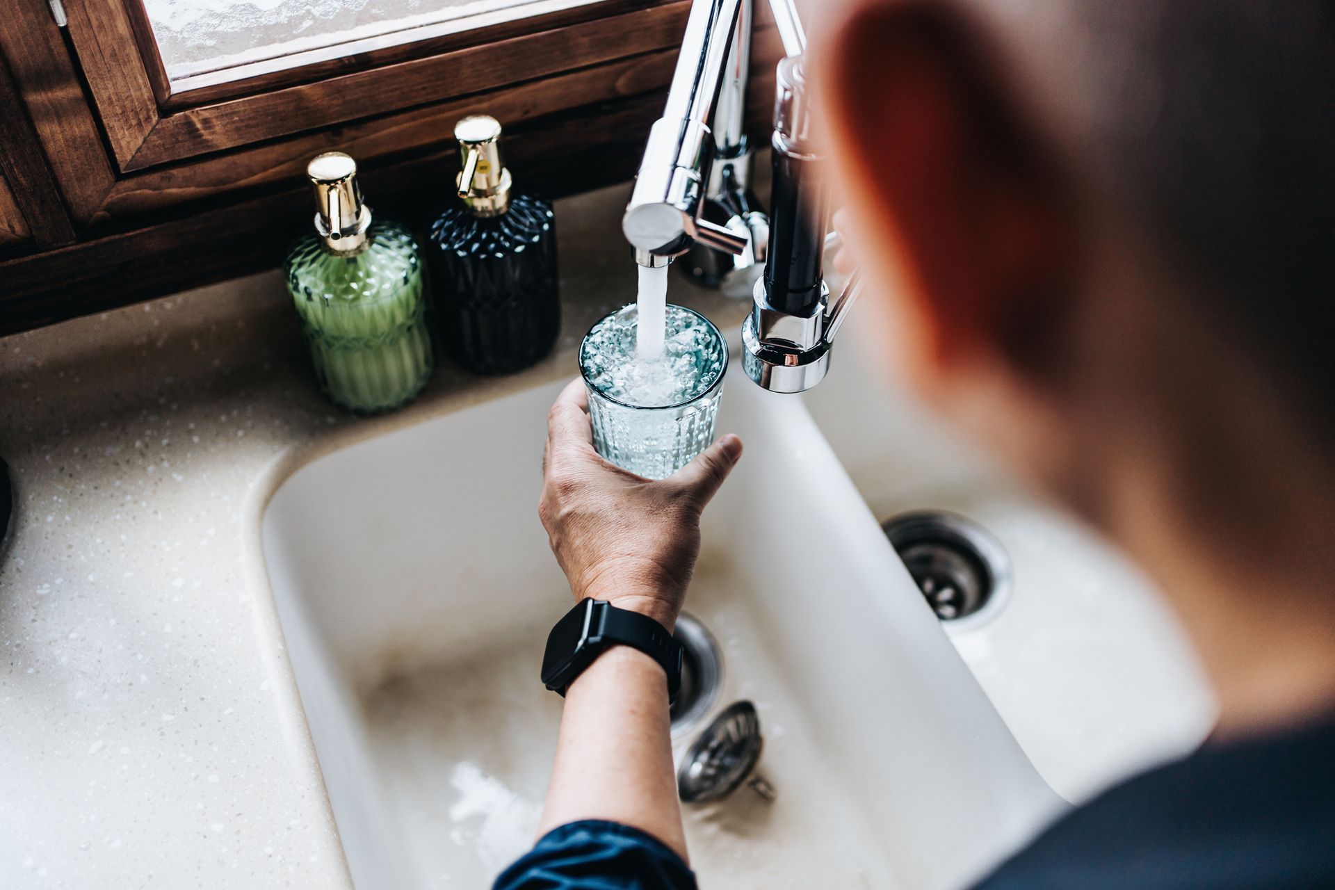 A person is pouring water from a faucet into a glass.