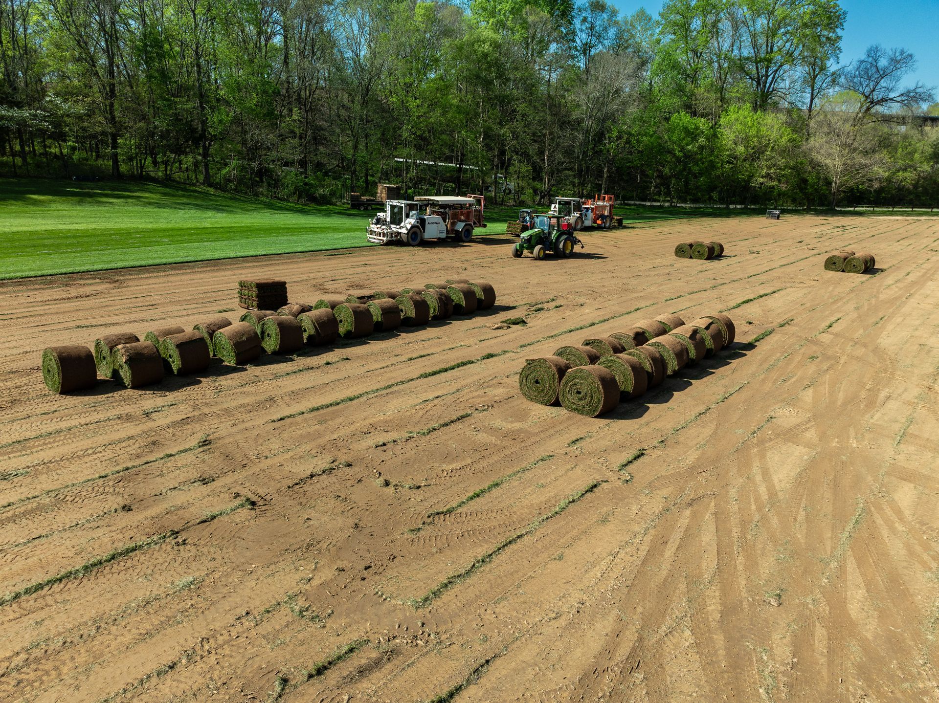 A field filled with rolls of grass and a tractor.