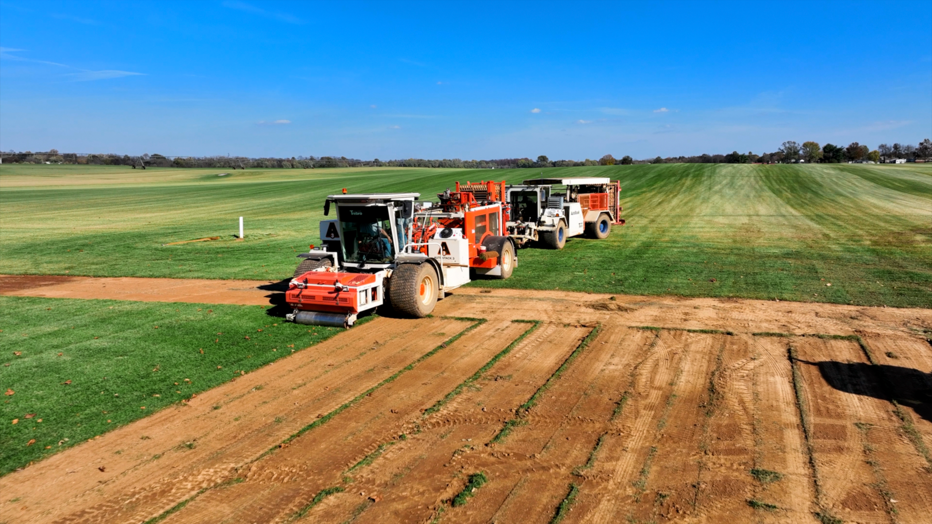 A row of tractors are working in a field of grass.