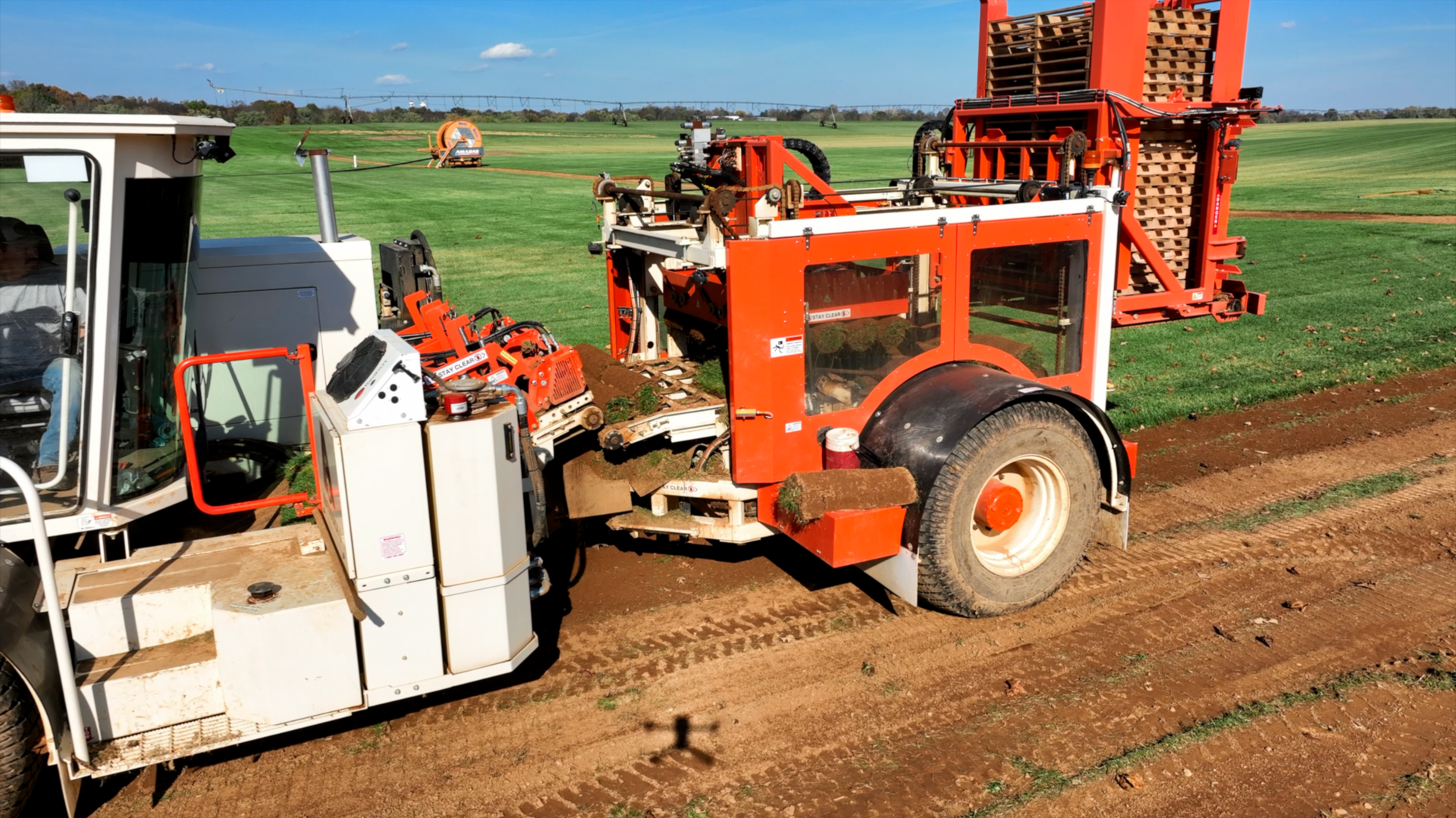 A tractor is driving down a dirt road next to a tractor in a field.