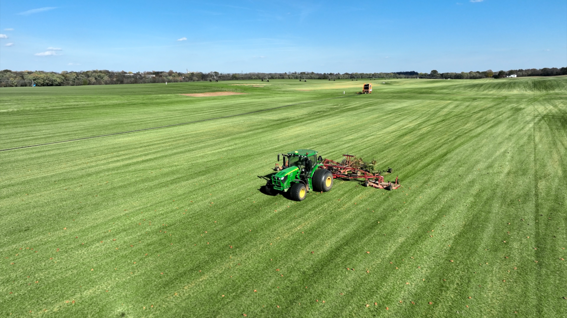 An aerial view of a green tractor plowing a grassy field.