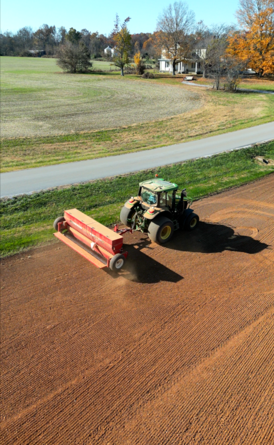 A tractor is plowing a field next to a road.