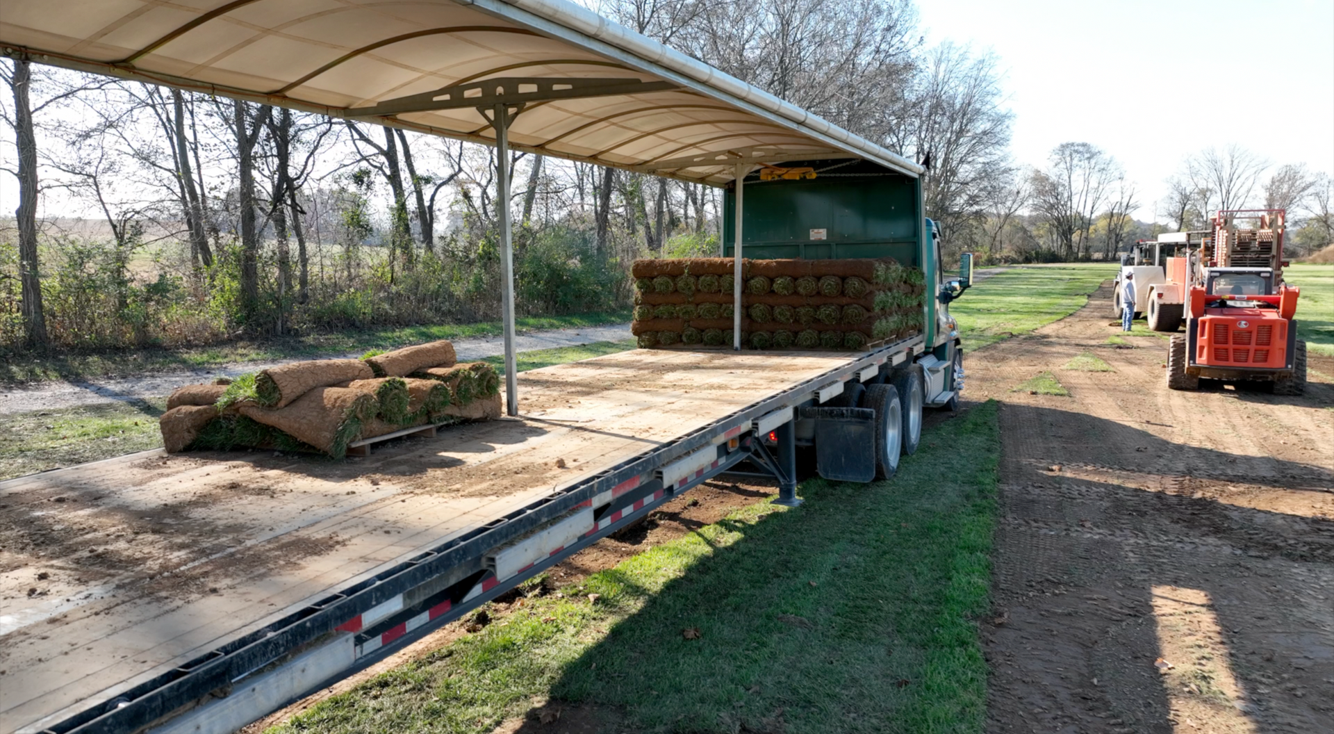 A truck is carrying rolls of grass on a trailer.