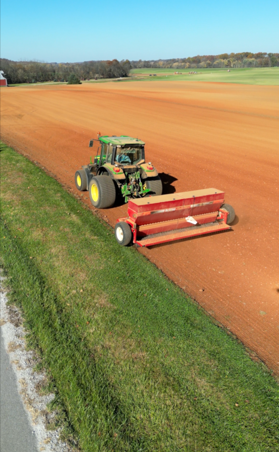 A tractor is plowing a field next to a road.