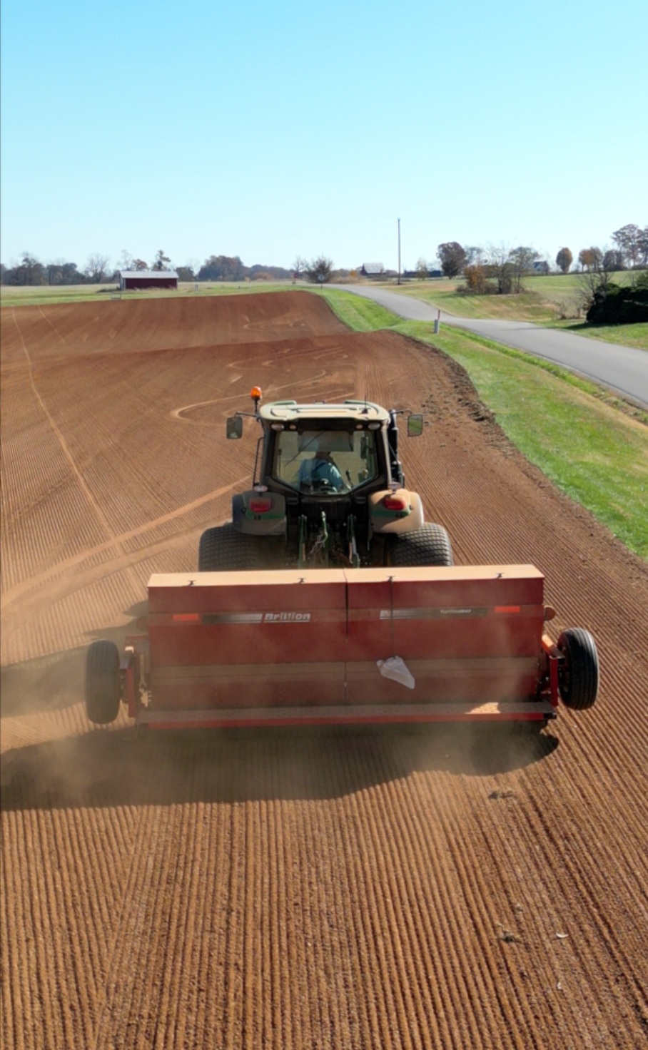 A tractor is plowing a field next to a road.