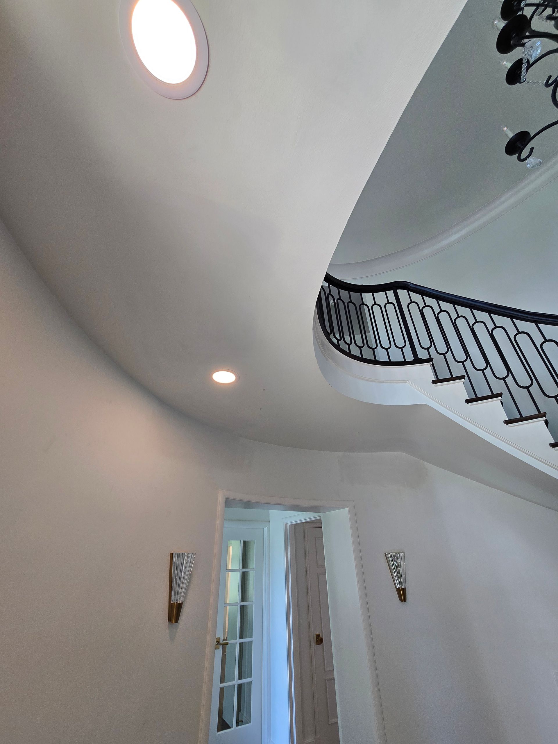 Curved white staircase and ceiling in a bright entryway with recessed lights and a glass door below