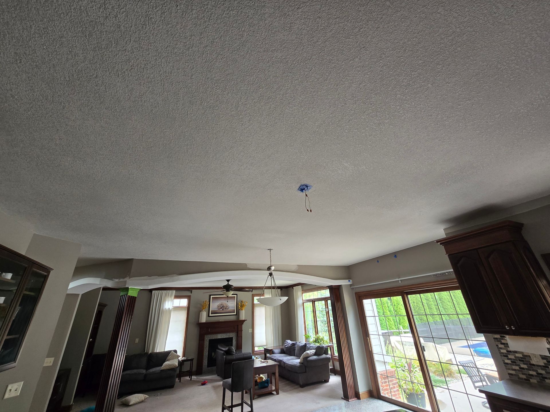 Living room with a high ceiling, fireplace, dark sofa, and large sliding glass doors opening to a patio.
