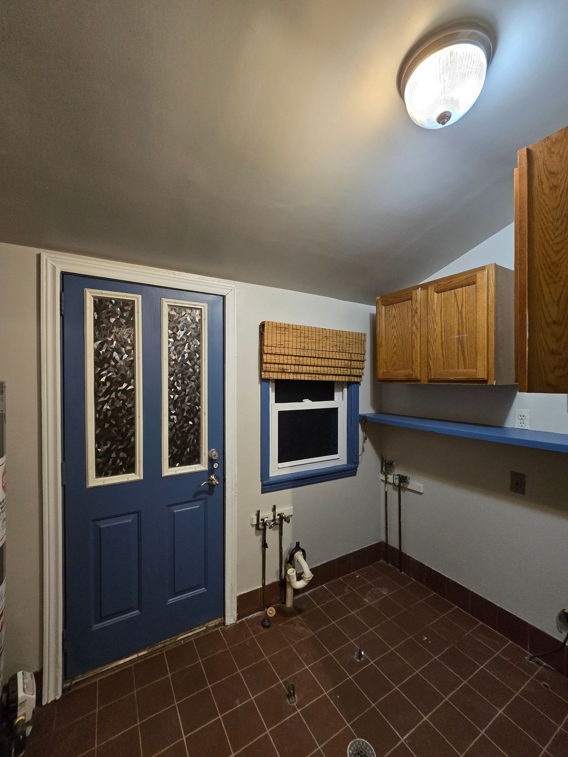 Small utility room with blue door, window, wood cabinets, and brown tile floor.