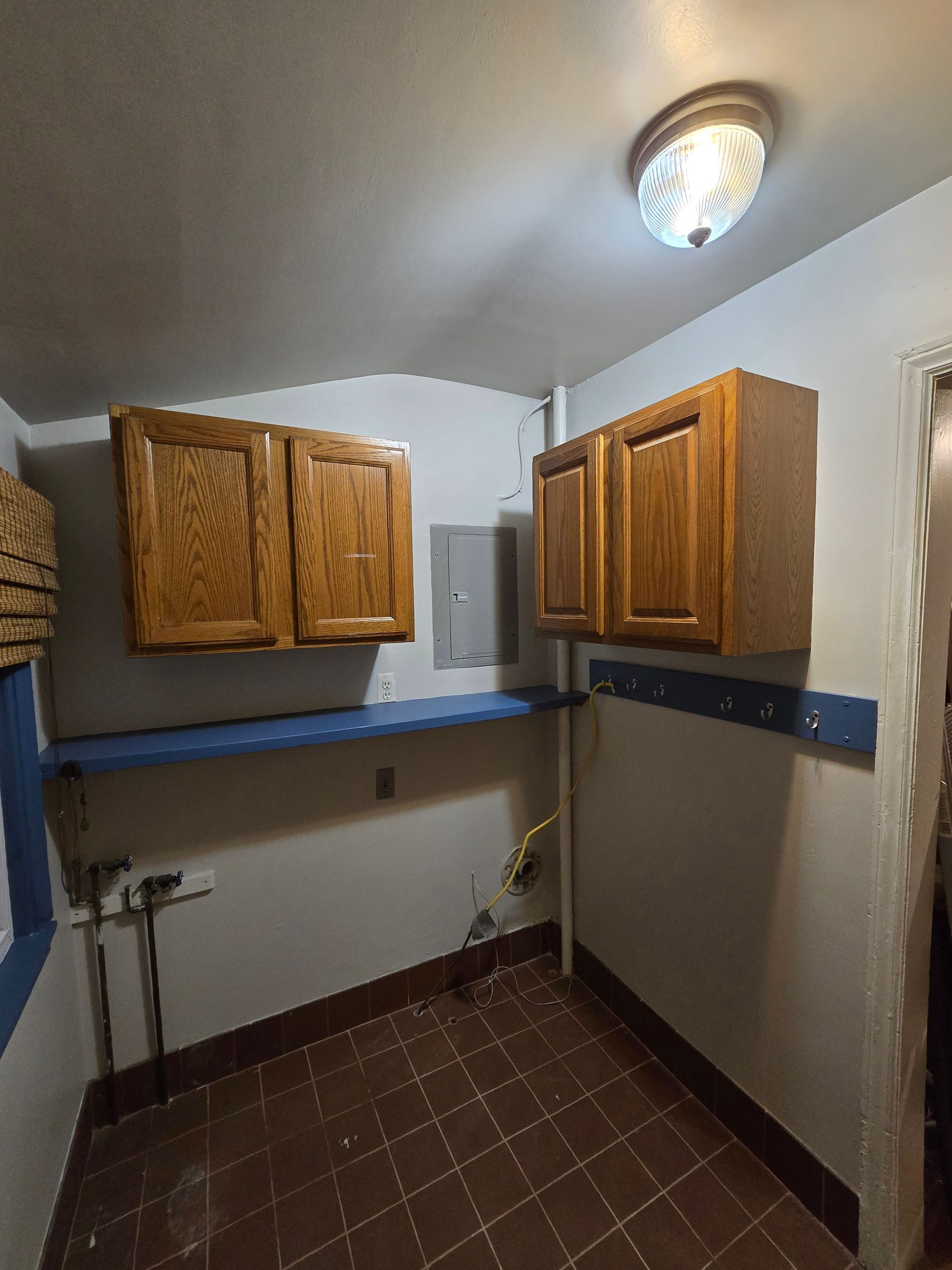 Small laundry room with wooden cabinets, blue countertop, tiled floor, and overhead light.