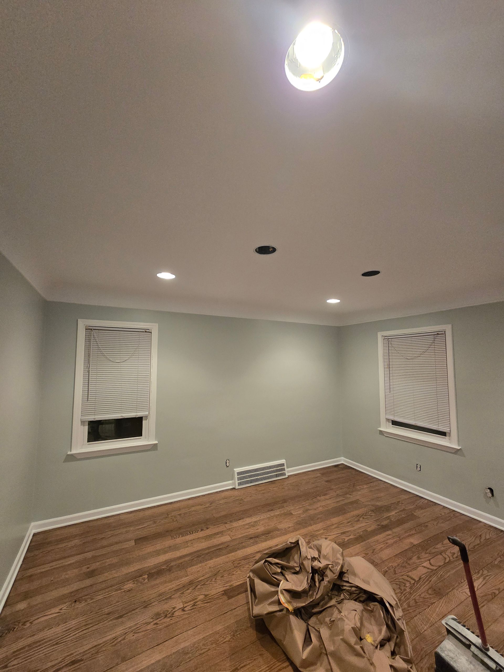 Empty gray room with recessed lights, wood floor, and covered windows; plastic on floor in foreground