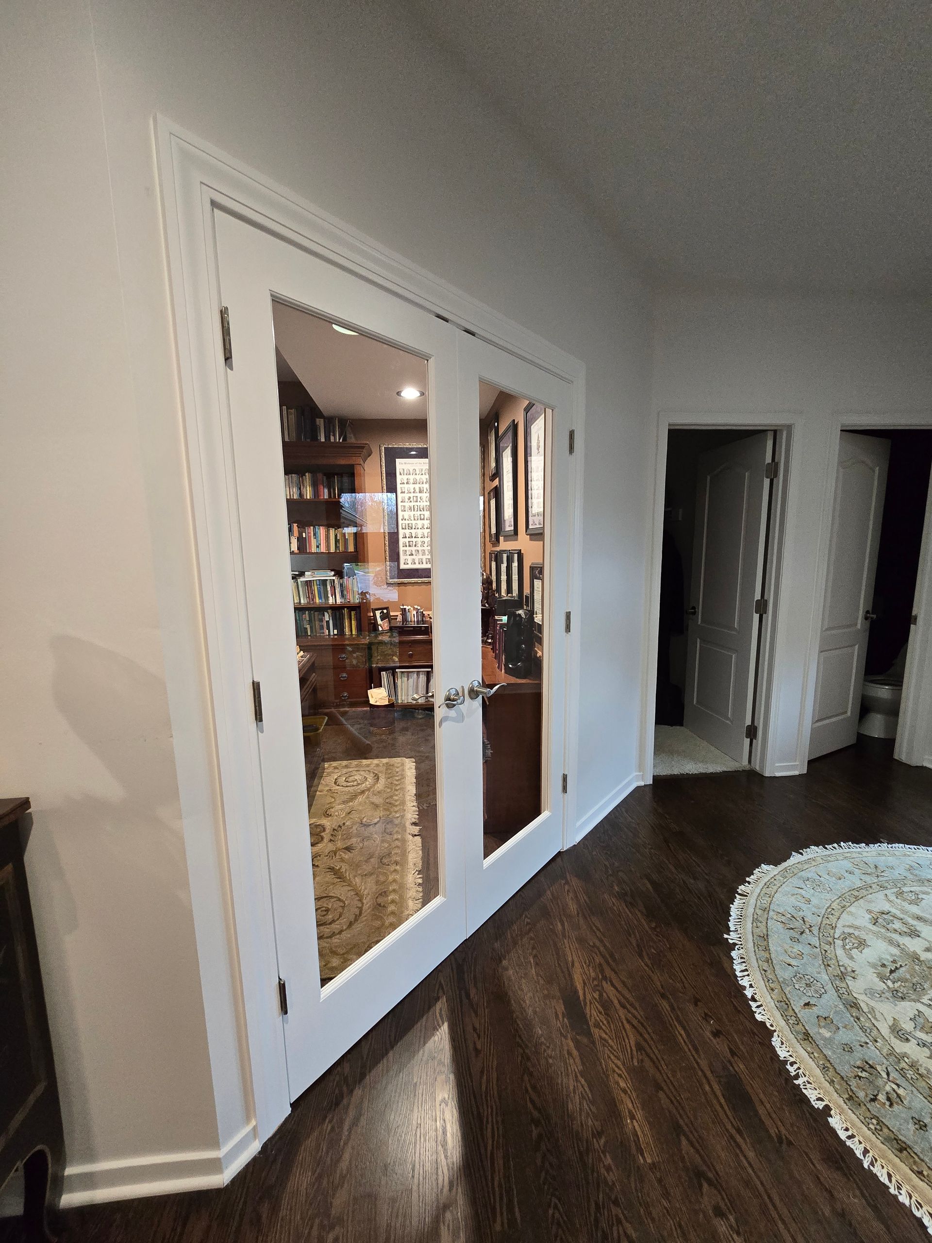 White double glass doors open to a warmly lit interior, beside a curved doorway and dark wood floor.