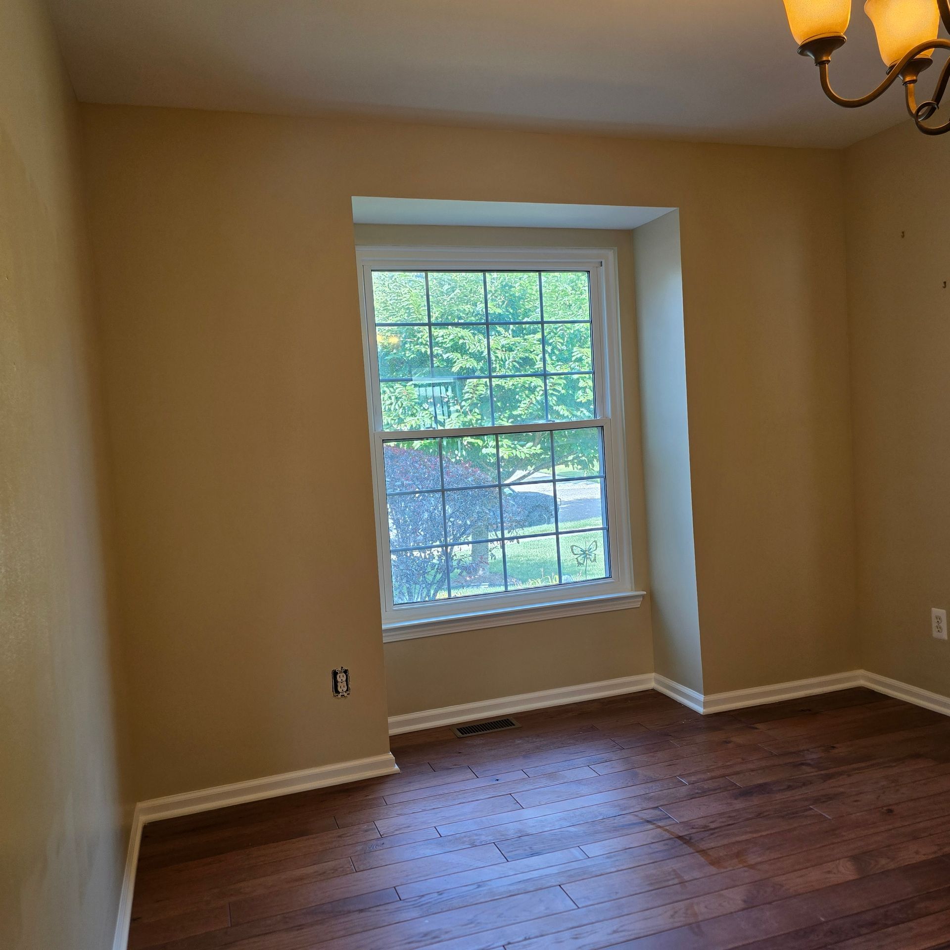 Empty beige room with hardwood floors and a window letting in daylight