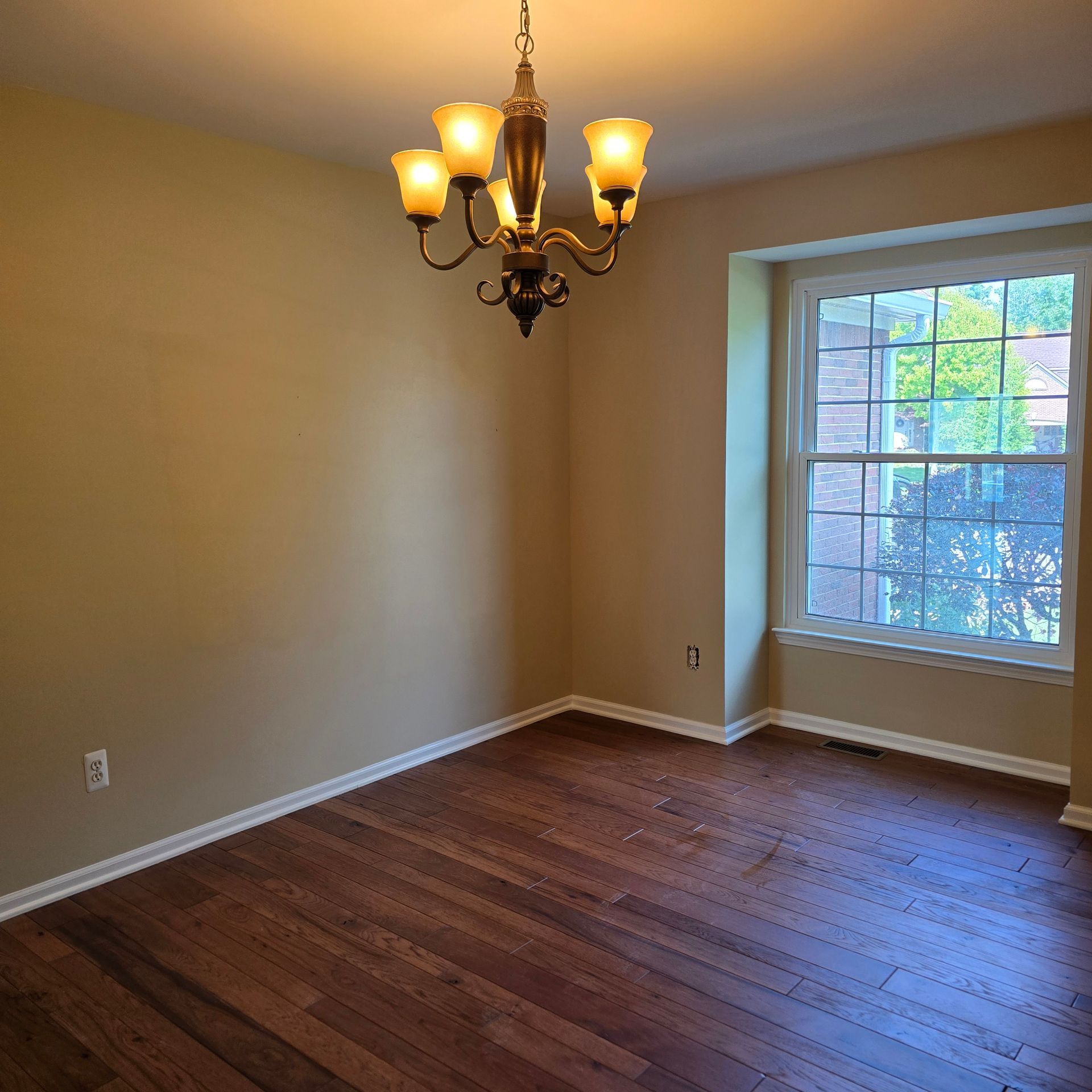 Empty dining room with hardwood floors, beige walls, a chandelier, and a large window.
