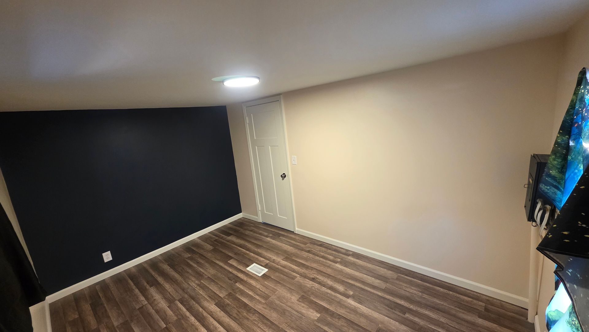 Empty room with dark accent wall, beige walls, wood floor, and ceiling light.
