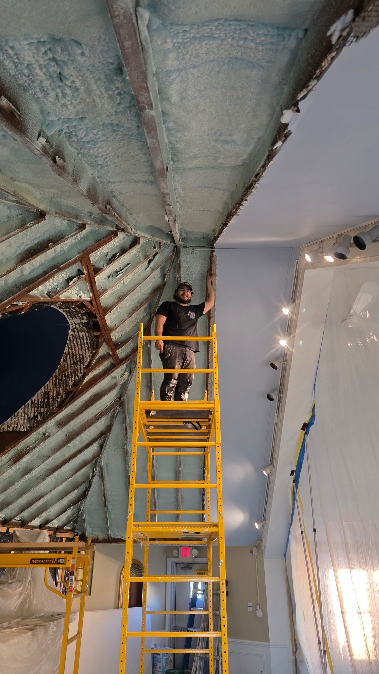 Worker on a yellow lift inspecting a curved, blue-gray ceiling inside a room under renovation.
