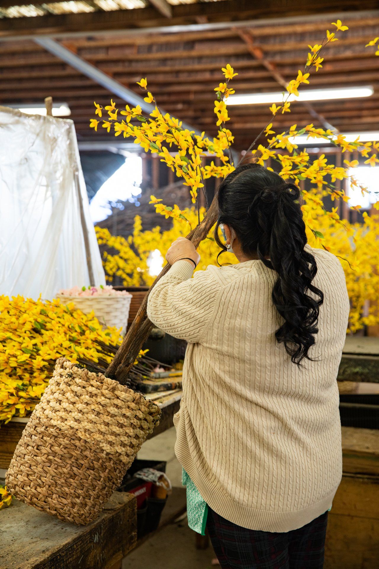 A woman is working on a bunch of silk plants in a warehouse.