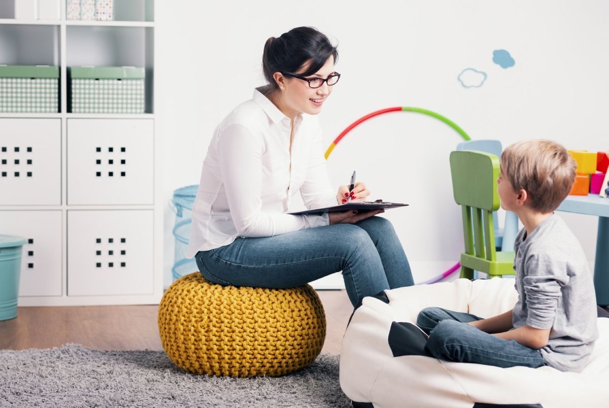 Woman in glasses and child in room, possibly counseling or therapy session; woman takes notes.
