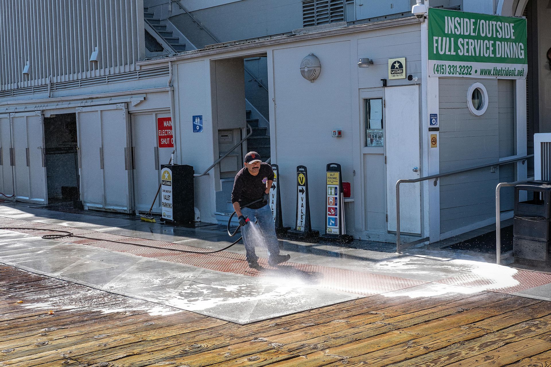 Person spraying water on a deck near a building with accessibility ramp, signs and the words 