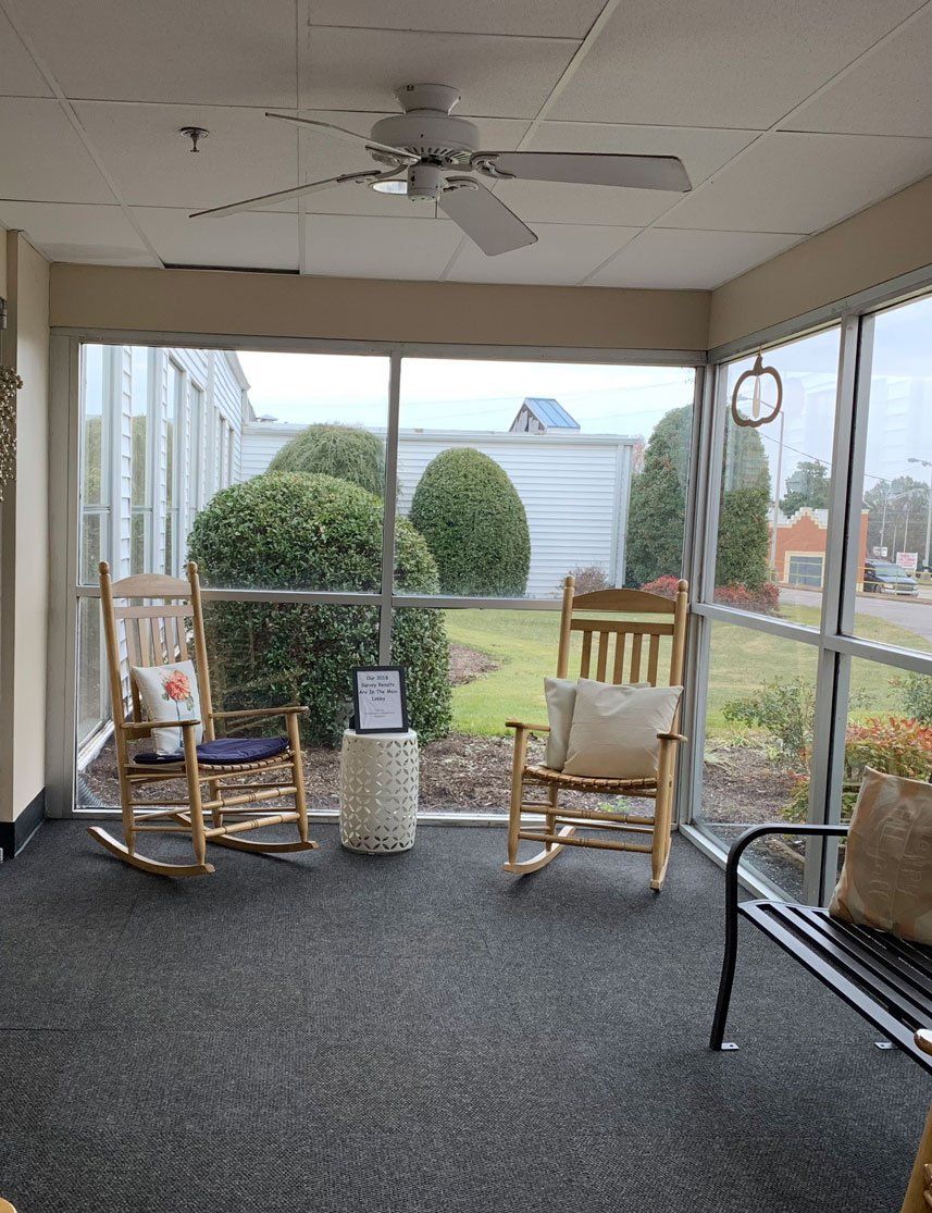 A screened in porch with rocking chairs and a ceiling fan.