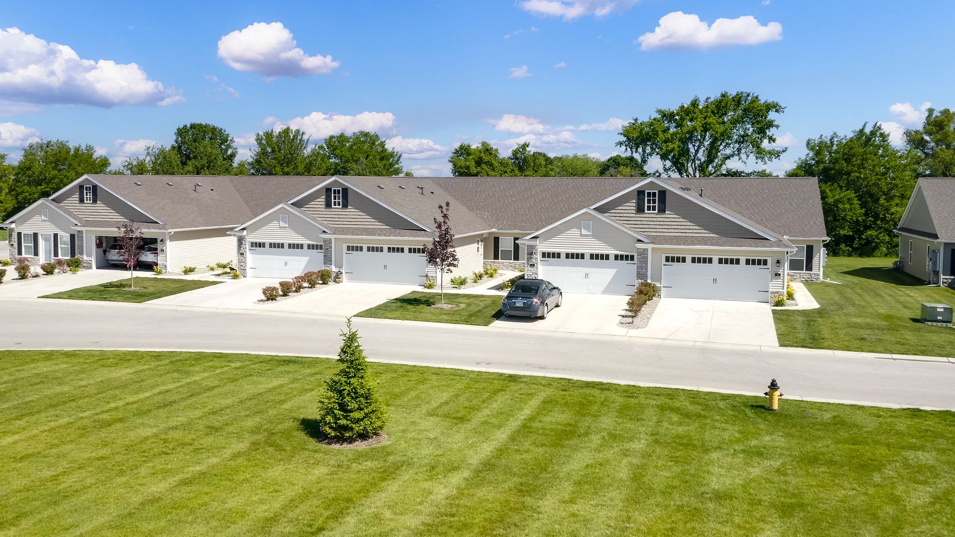 Row of white attached houses with garages on a green lawn under a blue sky.