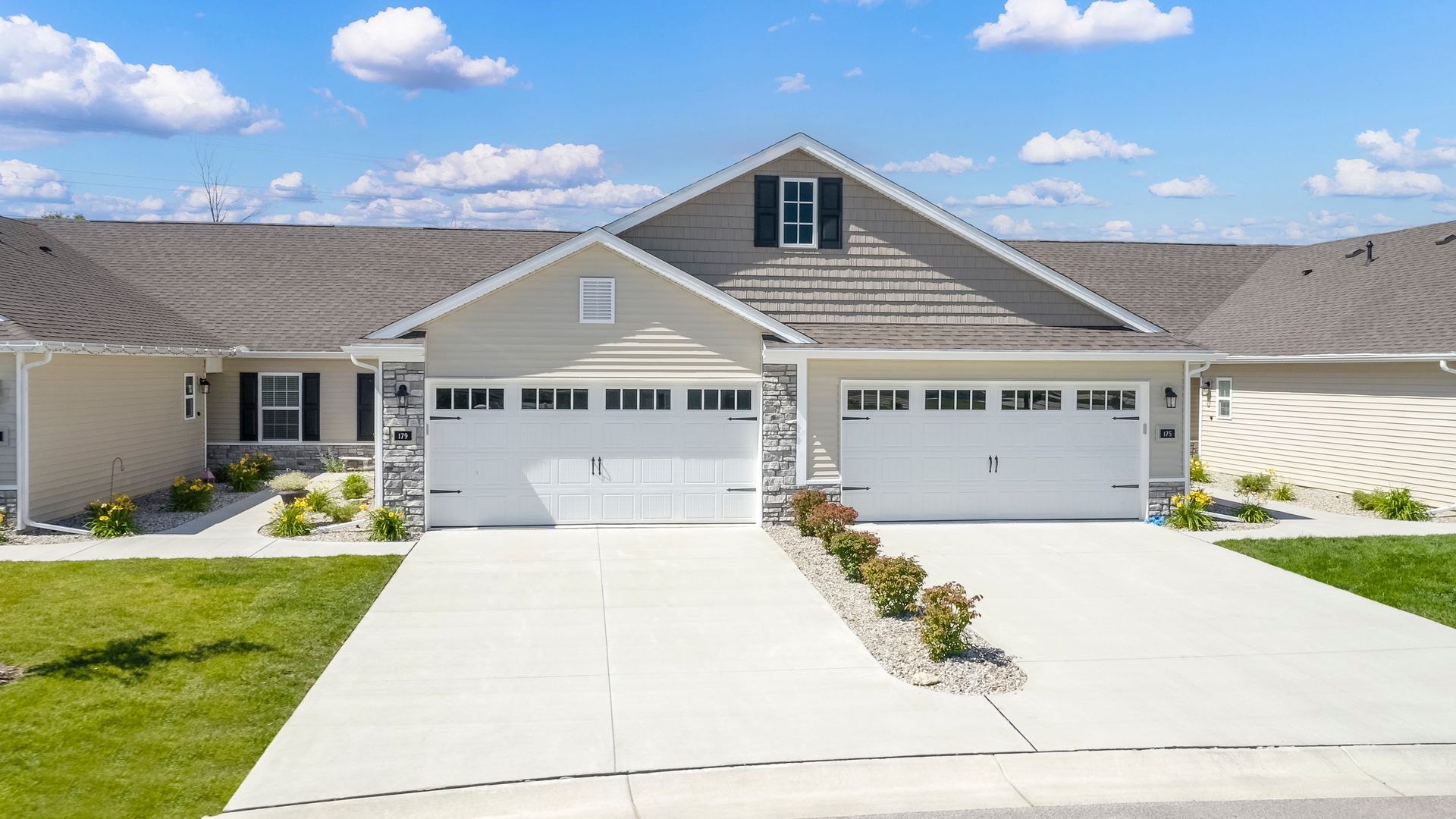 Townhouse exterior with two attached garages, light gray siding, and a blue sky.