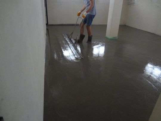 Un uomo sta stendendo del cemento sul pavimento con una cazzuola.