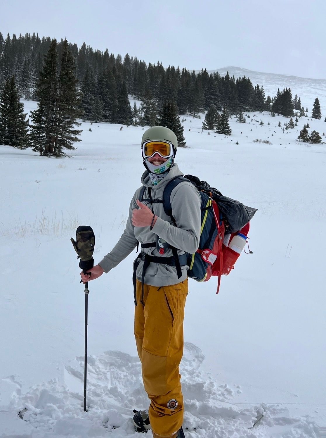 Person on skis in snow, wearing goggles, backpack, and holding ski poles in a mountainous setting.