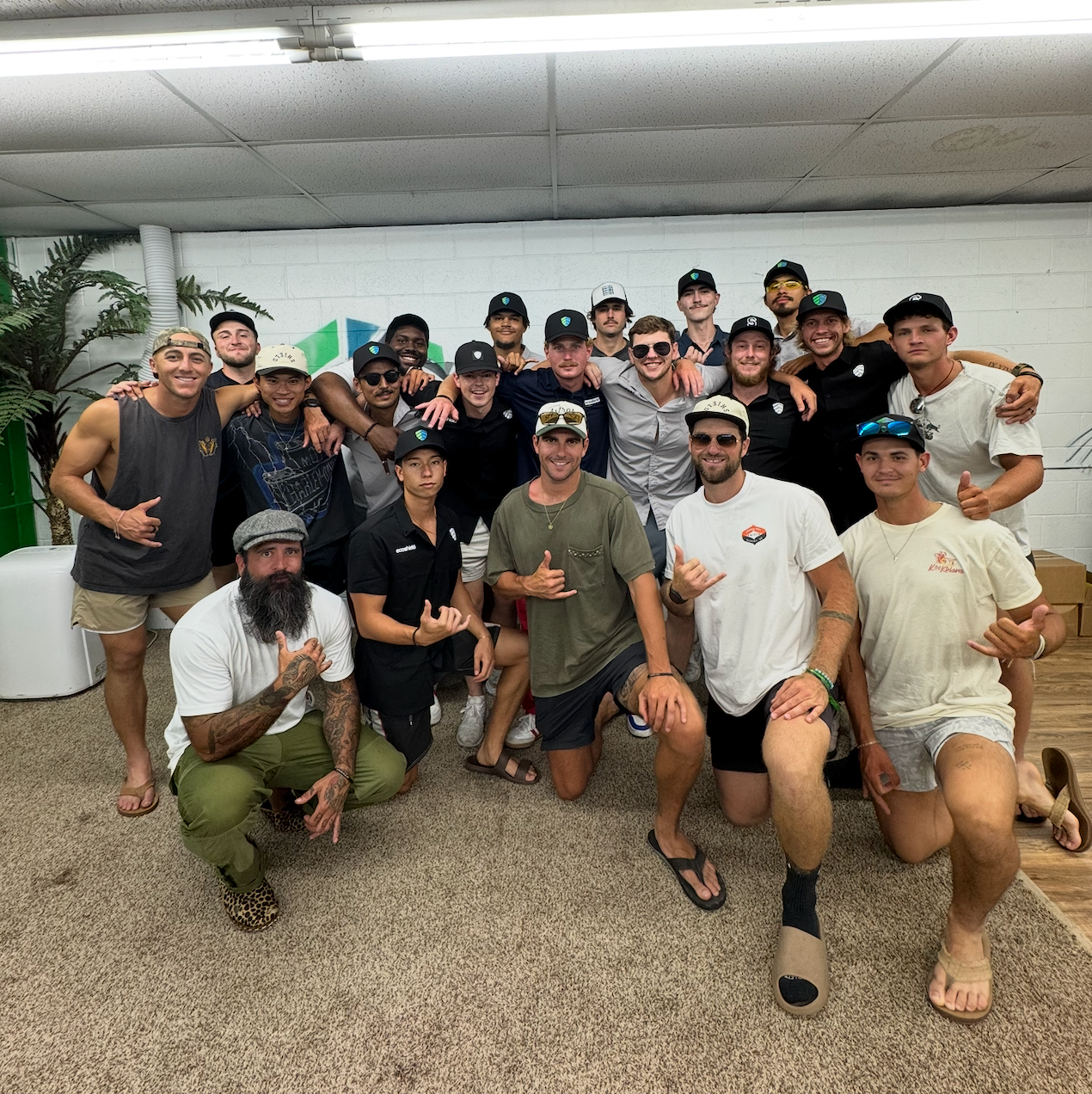 Group of diverse people posing indoors, some giving shaka signs.