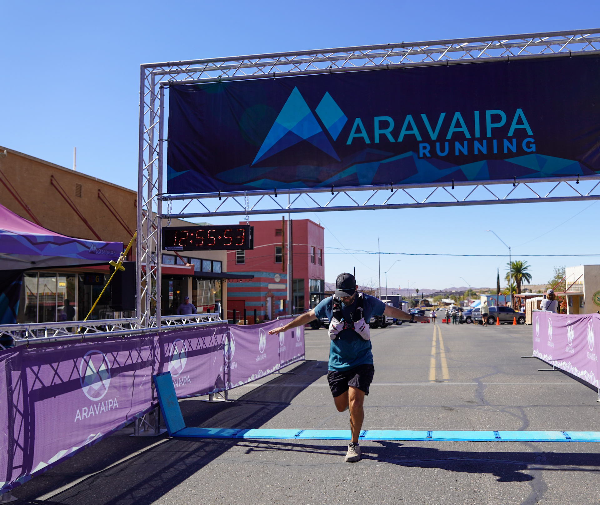 Runner crossing finish line under a banner, time displayed: 7:35:54. Blue and purple colors.