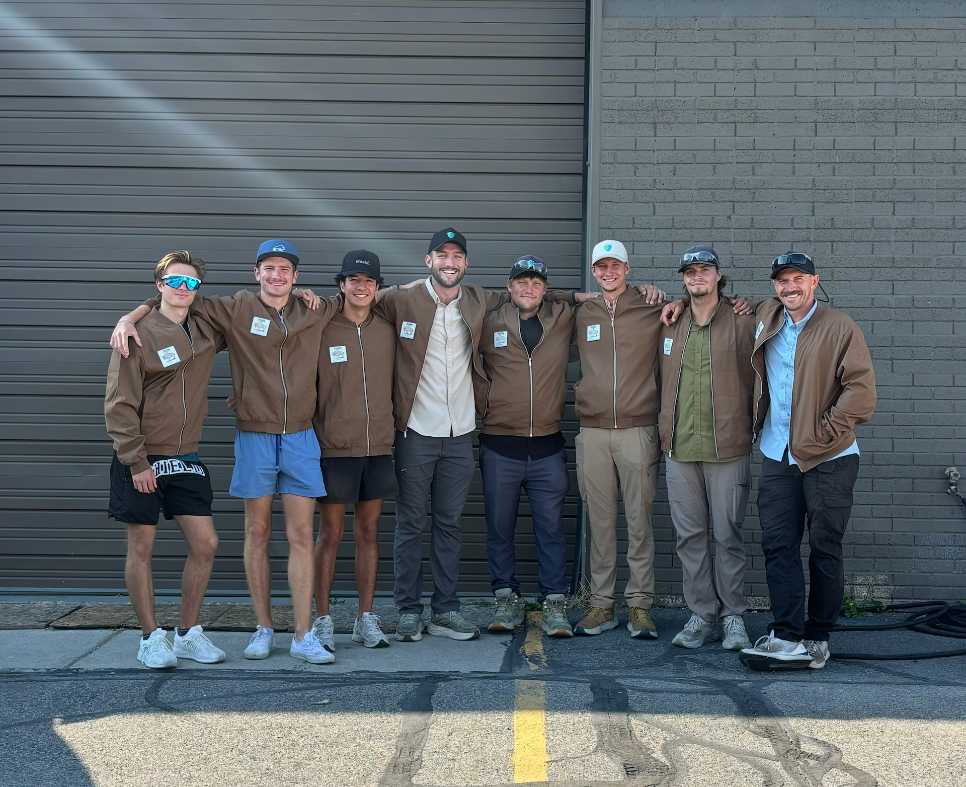 Man spraying pesticides on bushes and grass in a yard, wearing a hat, safety glasses, and gloves.