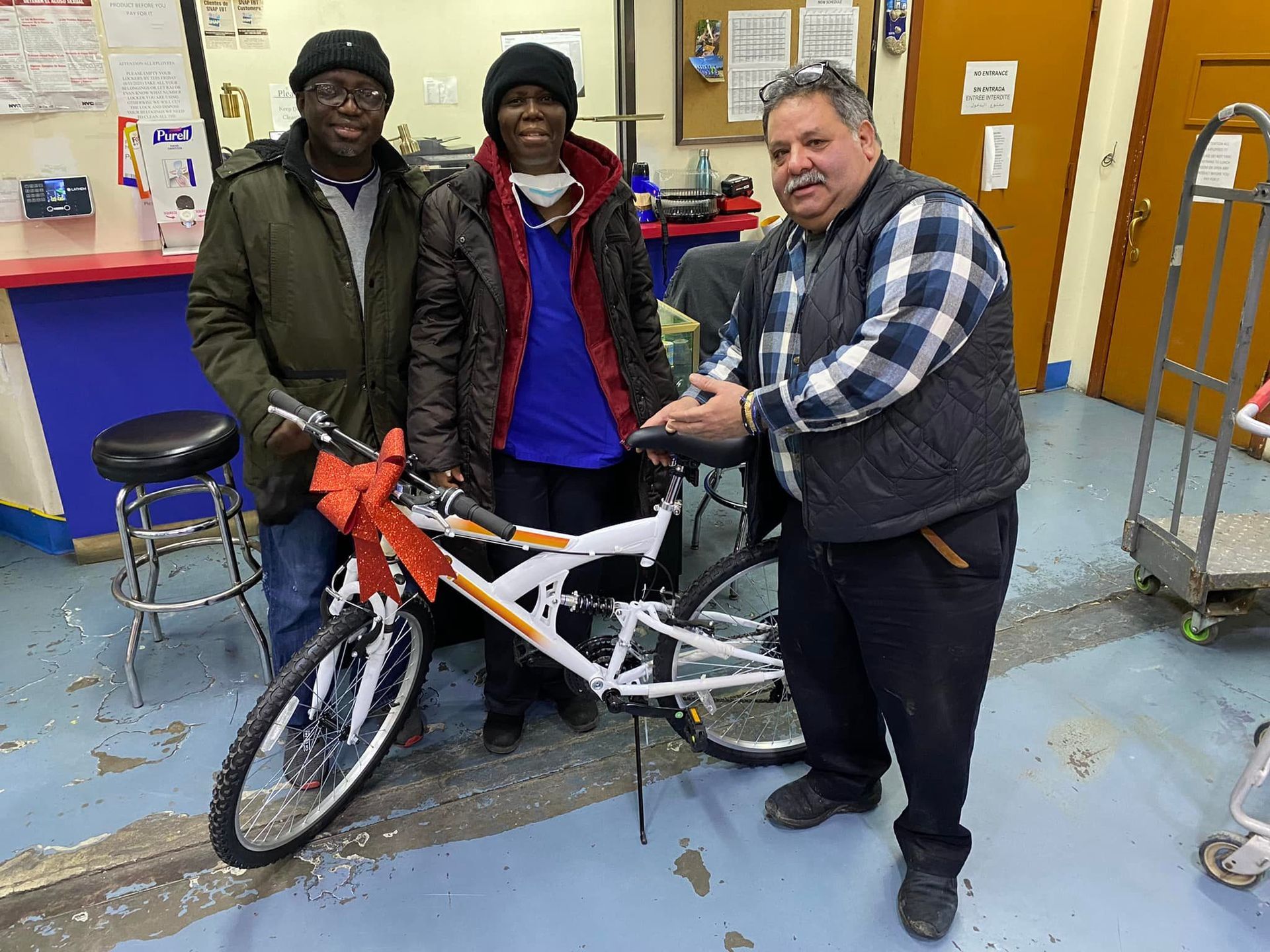 Three men are standing next to a bicycle with a red bow on it.