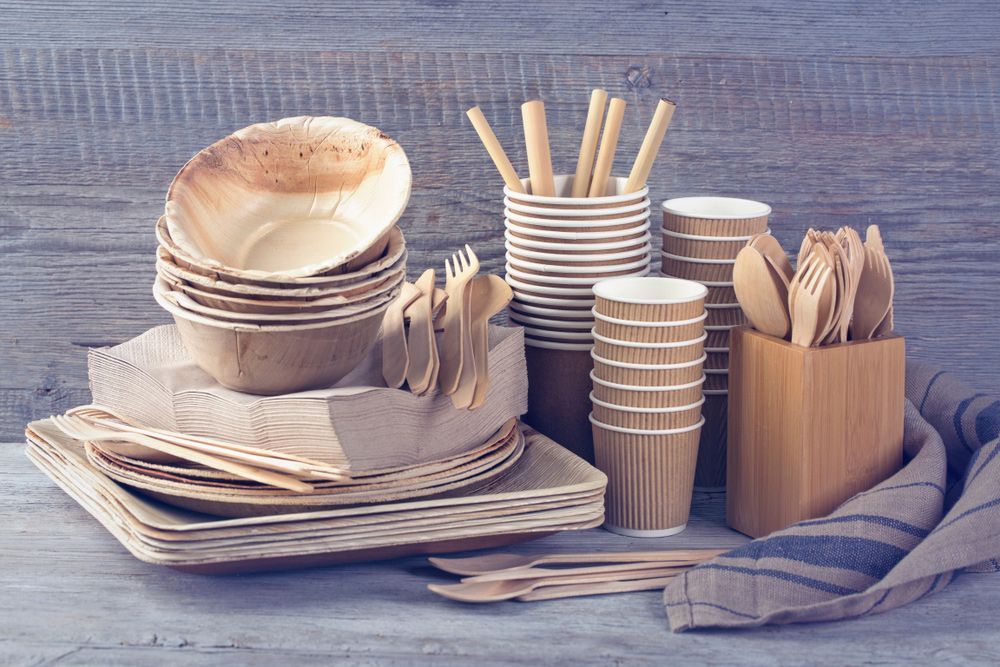A wooden table topped with paper plates, cups, utensils, and straws.