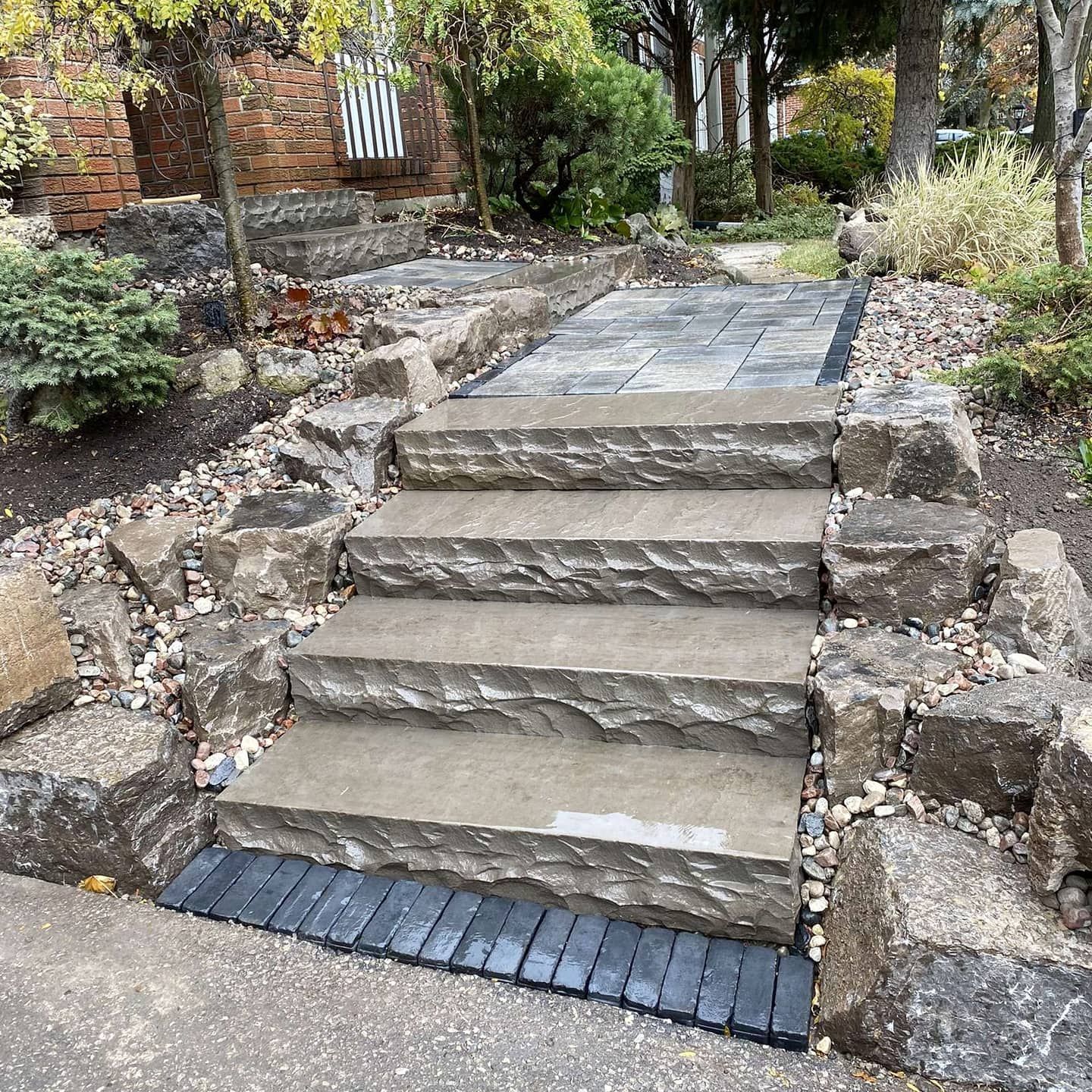 Stone steps leading up to a paved path, surrounded by rocks and greenery.