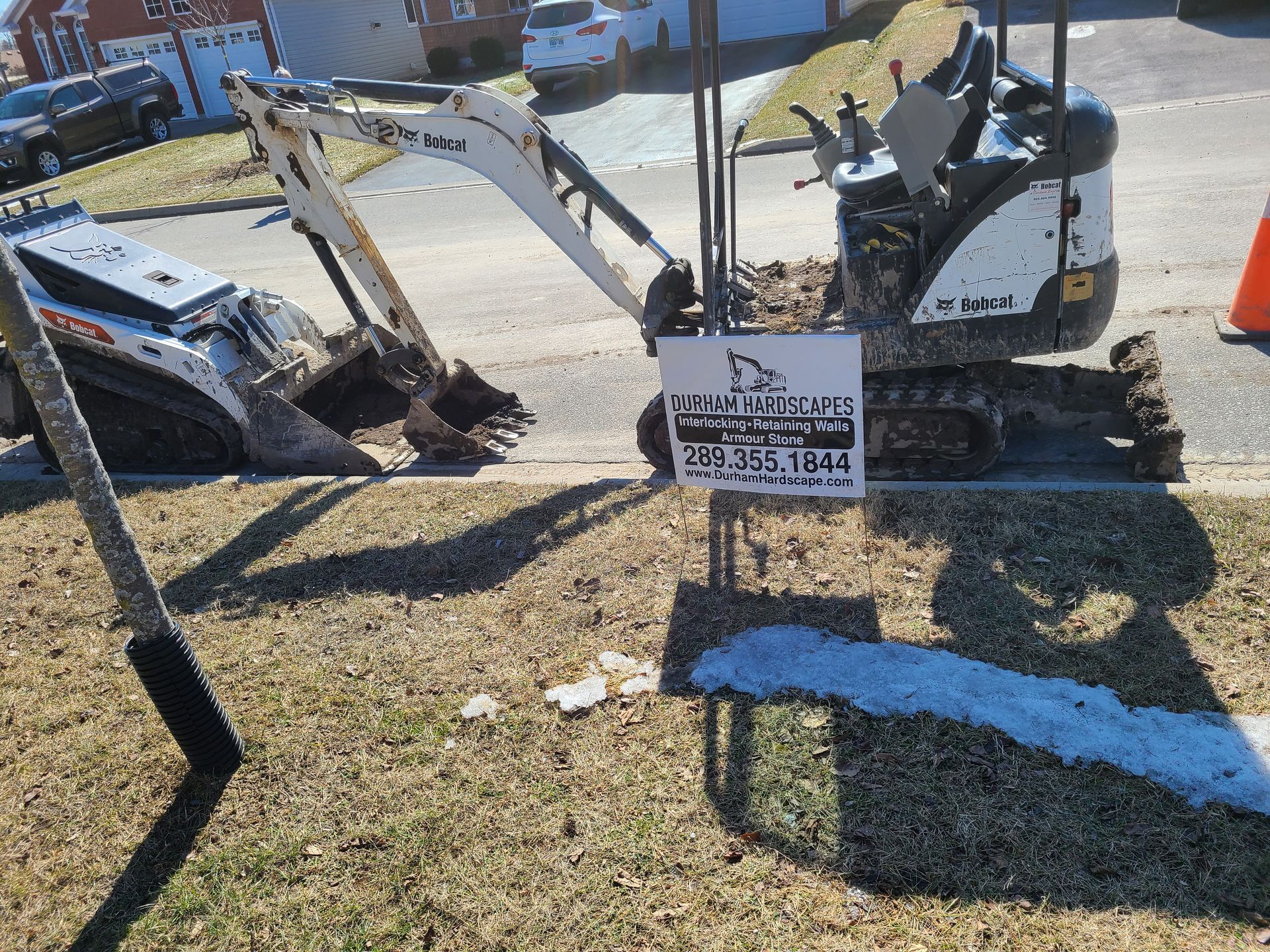Bobcat mini excavator and skid steer on a residential lawn, with a sign containing contact information.