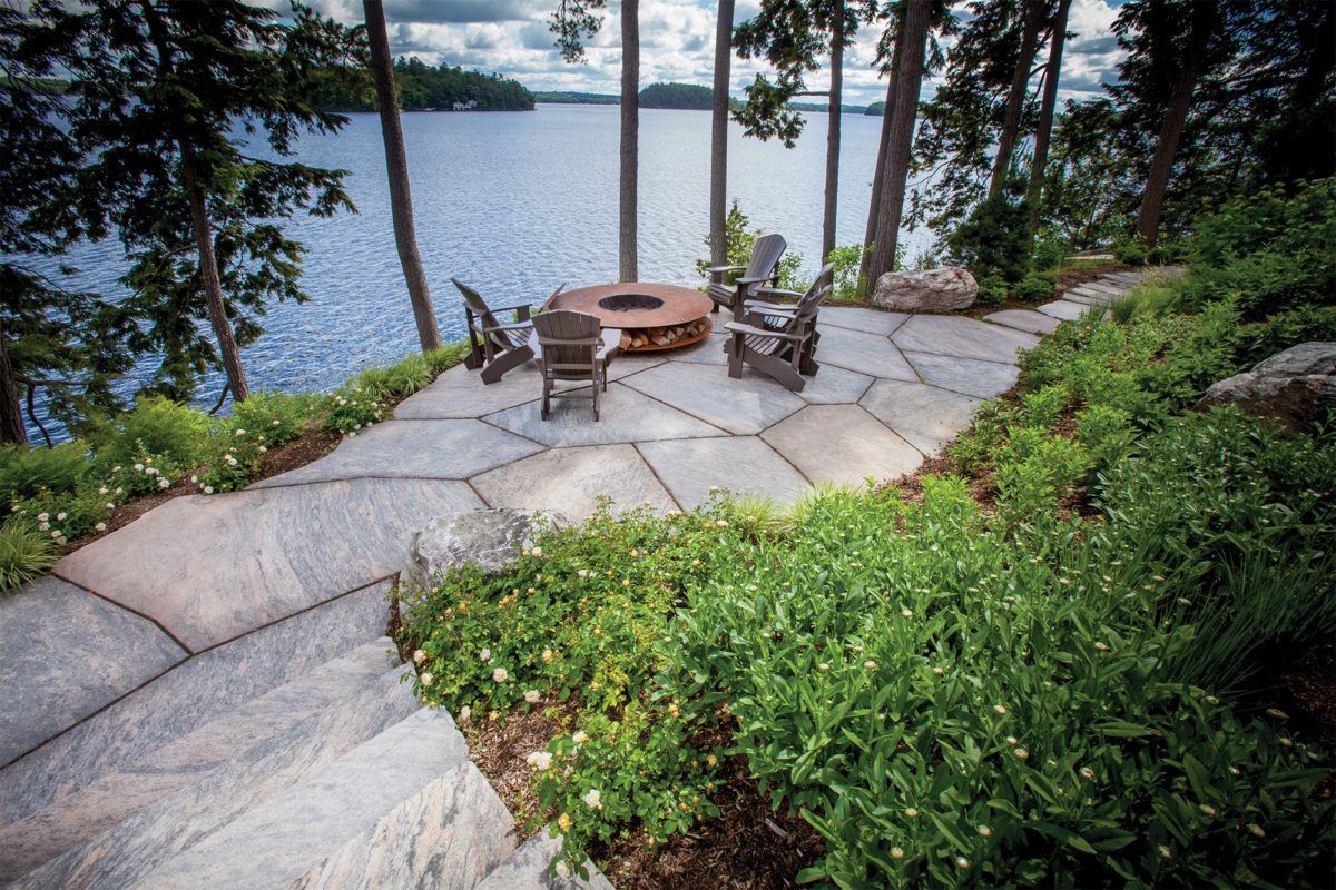 A patio with a fire pit and chairs overlooking a lake.
