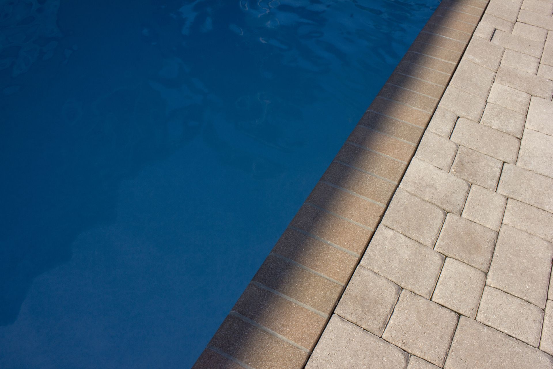 Blue pool water next to a tan brick patio.