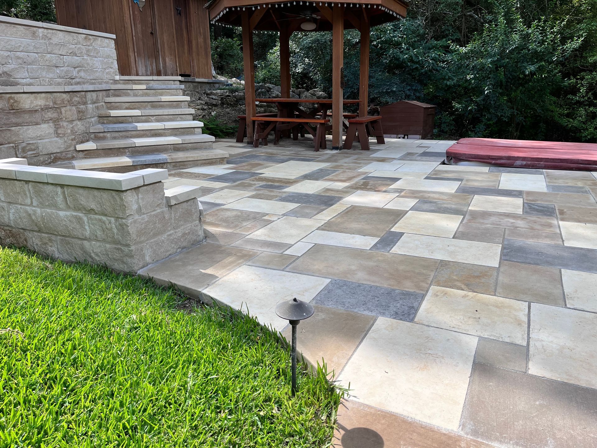 A stone patio features a multi-level retaining wall, stone steps, and a wooden gazebo with seating.