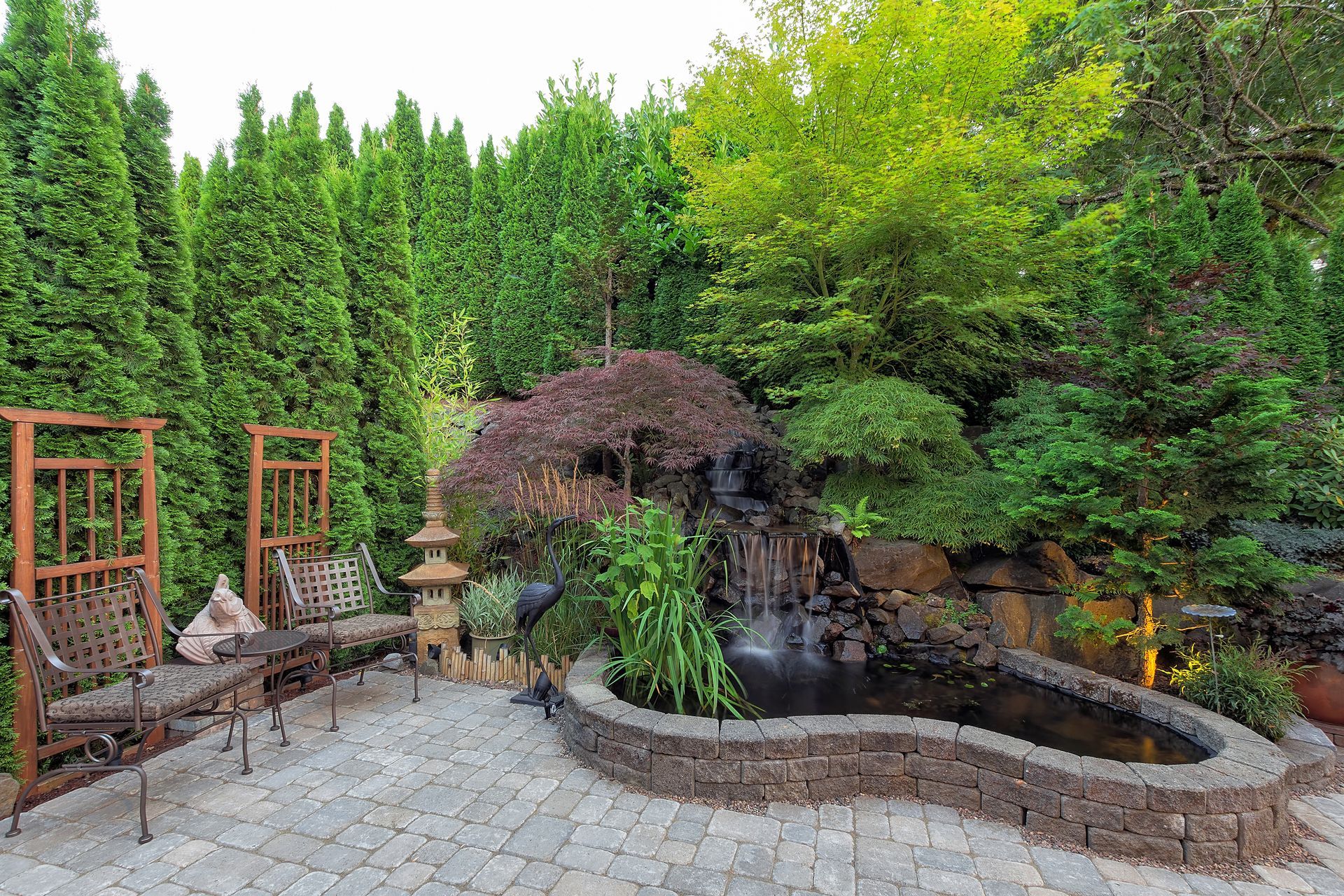 A patio with a pond and a waterfall in the middle of a forest.