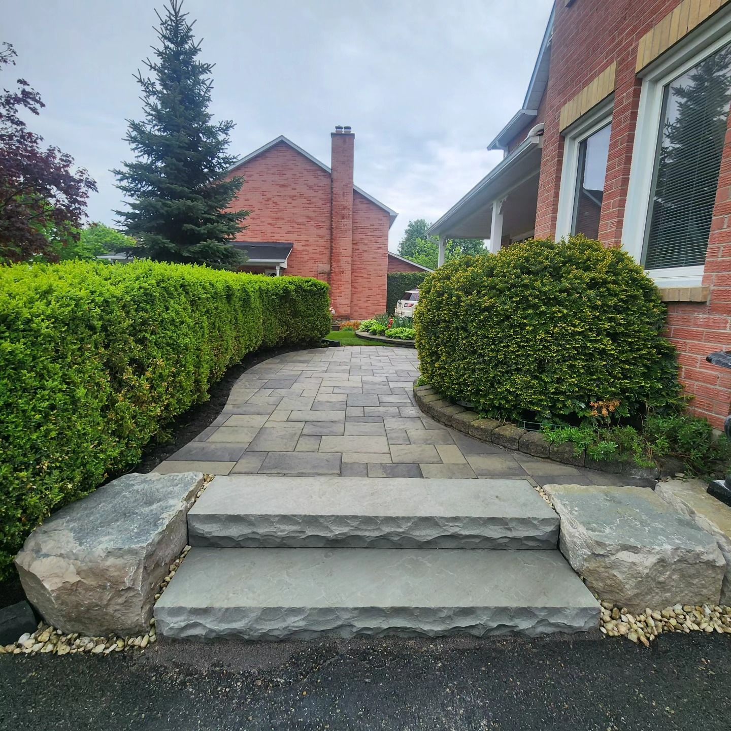 Stone steps lead to a brick house, flanked by bushes and a paved walkway.
