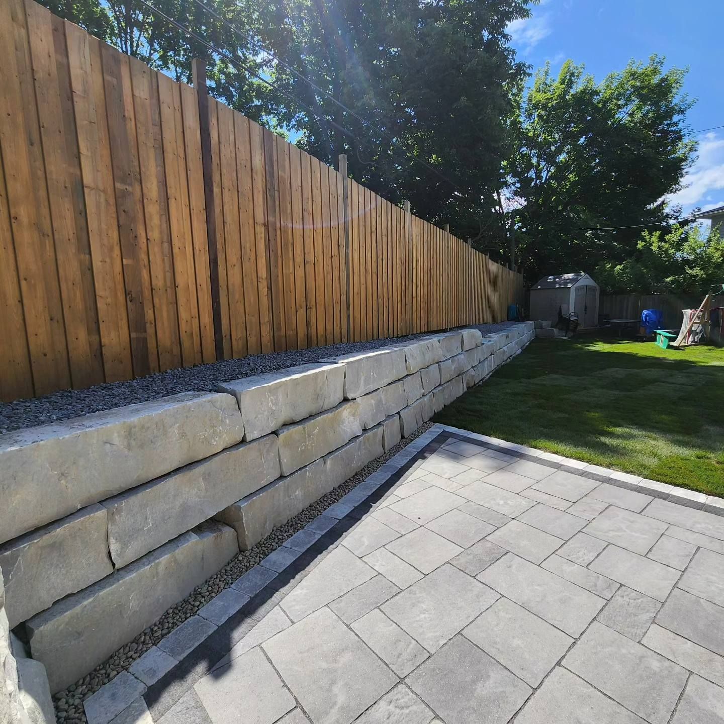 A wooden fence surrounds a brick wall in a backyard.