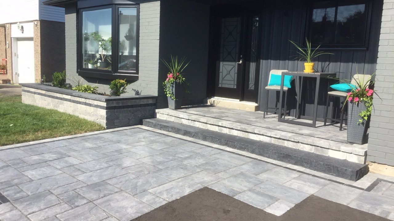 Gray paver patio and steps leading to a dark gray house with a small patio table and planters.
