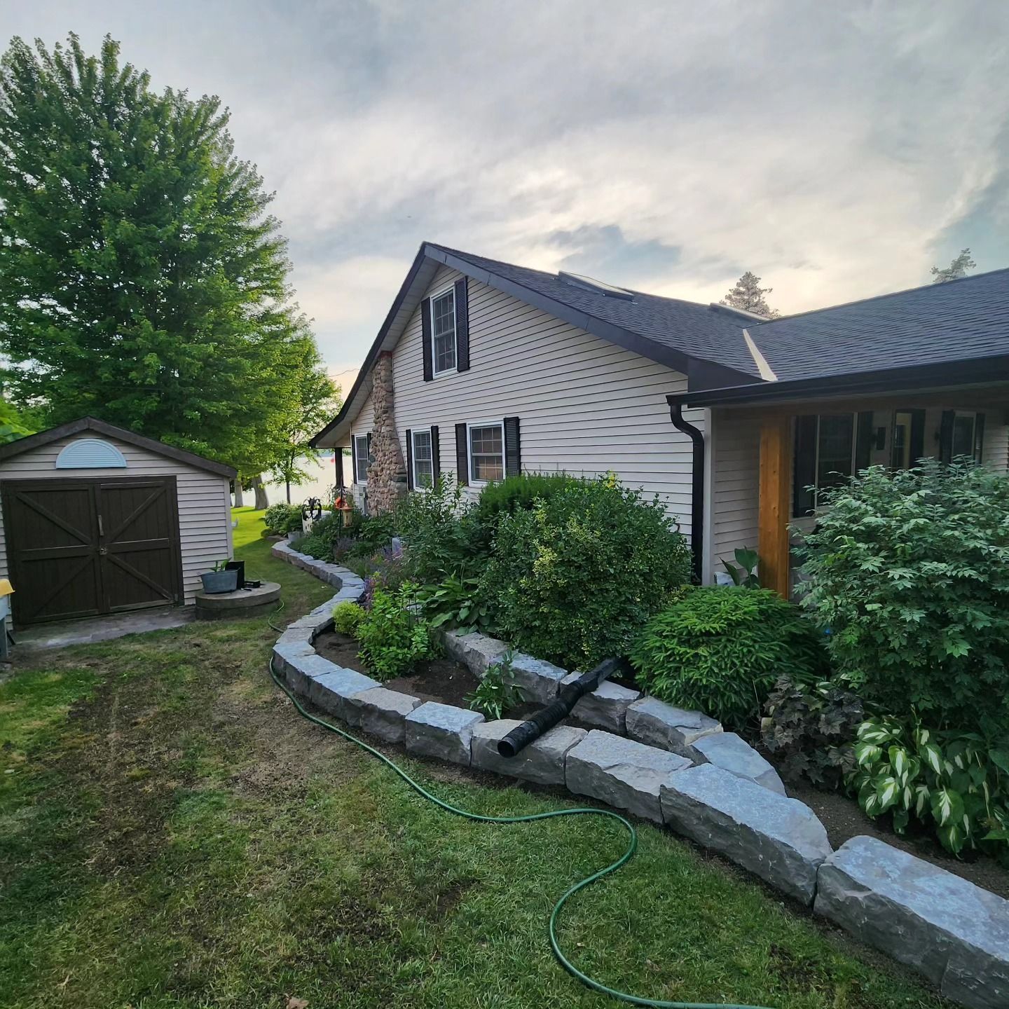 A house with a hose in front of it and a shed in the backyard.