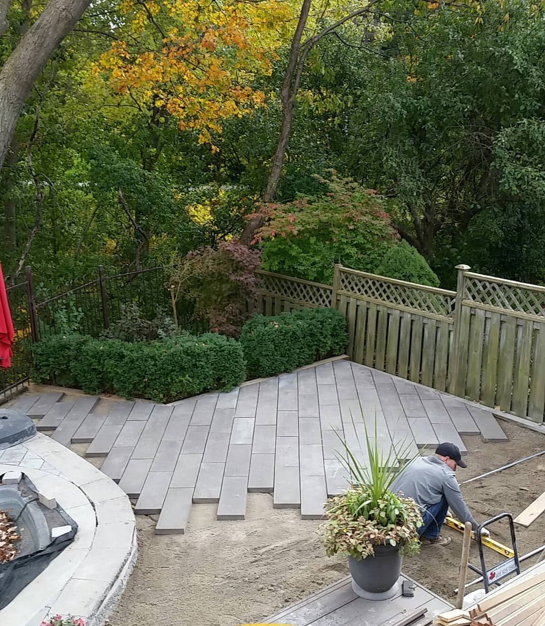 A man is laying bricks on a patio in a backyard.