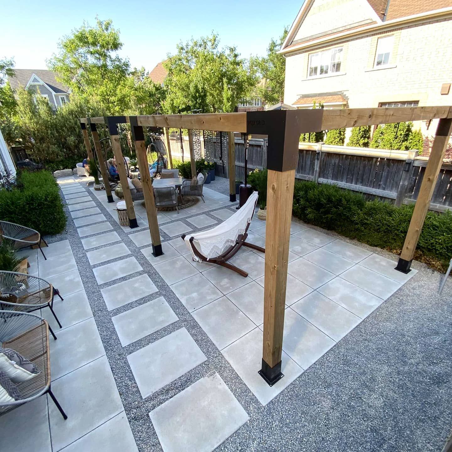 Outdoor patio with wooden pergola, stone pavers, gravel, chairs, and a hanging chair.