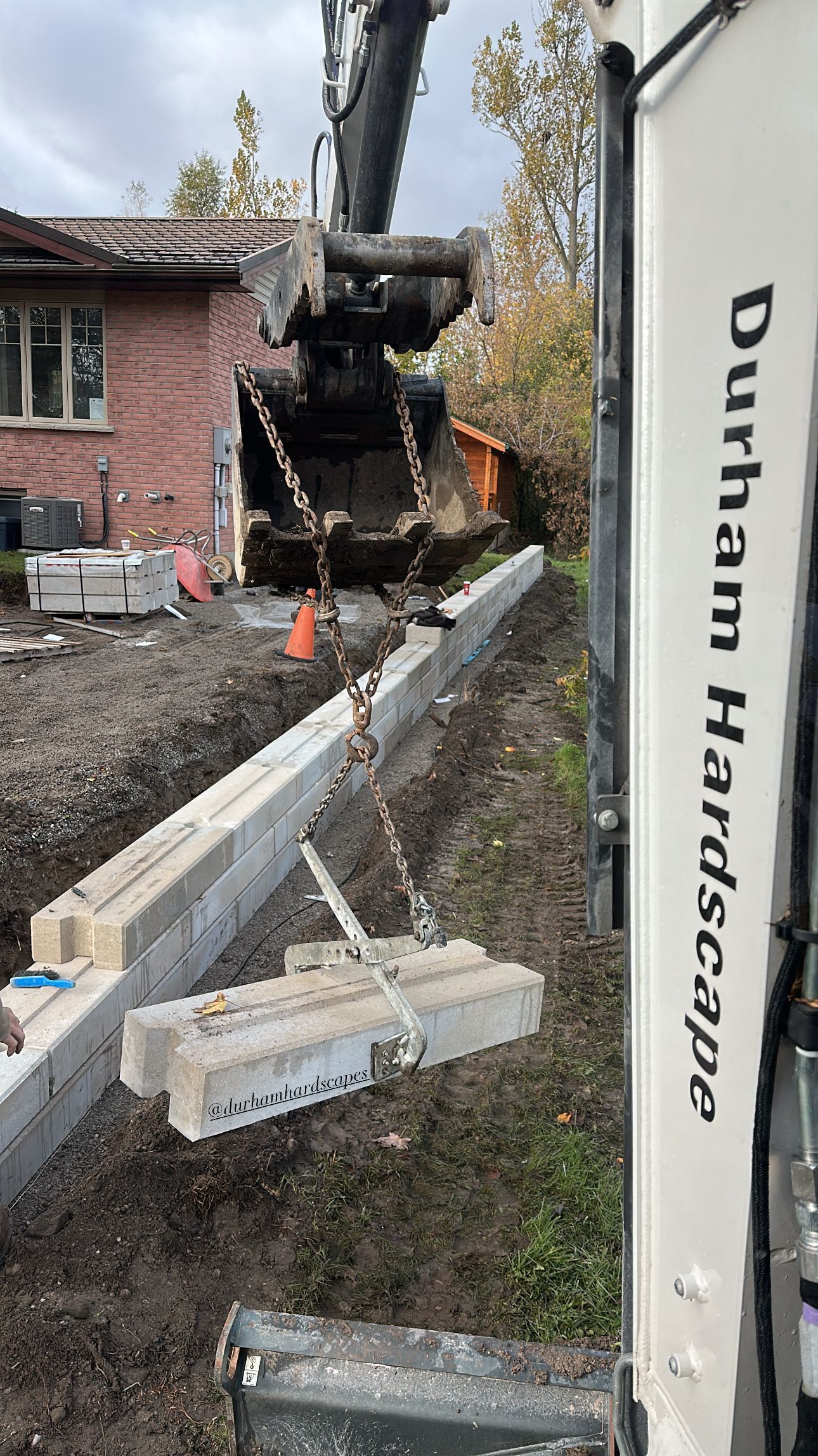 Excavator lifting concrete blocks for a retaining wall construction project.
