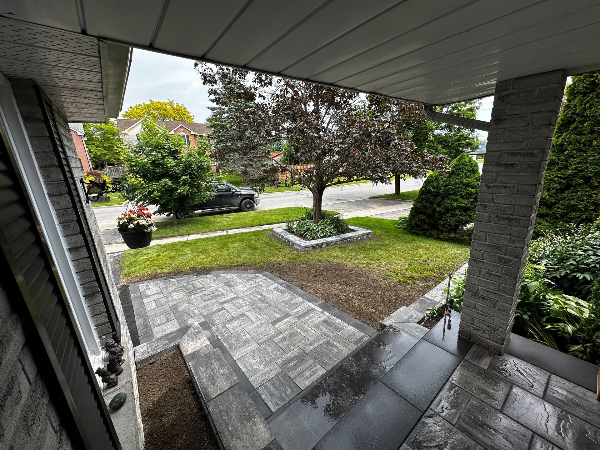 Stone steps and porch leading to a front yard with a tree and a car parked on the street.